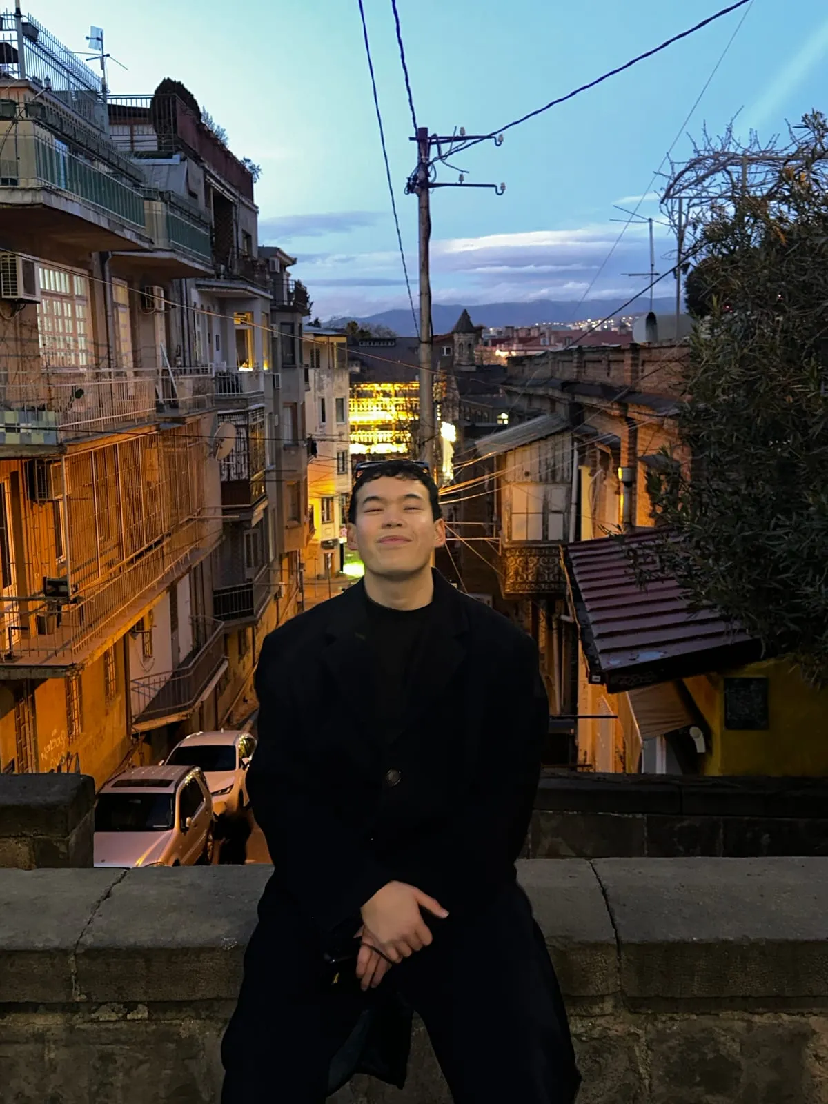Anuar, sitting on a stone wall above a hillside street at dusk